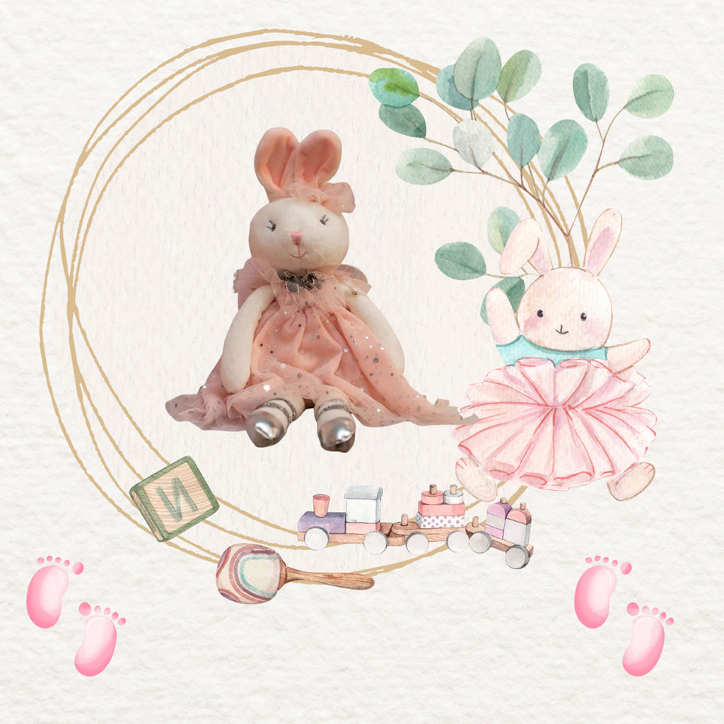 A watercolor-style nursery illustration featuring two pastel bunny figures in pink dresses, a small toy train, a pink rattle, baby footprints, and a decorative oval frame on a textured off-white background.