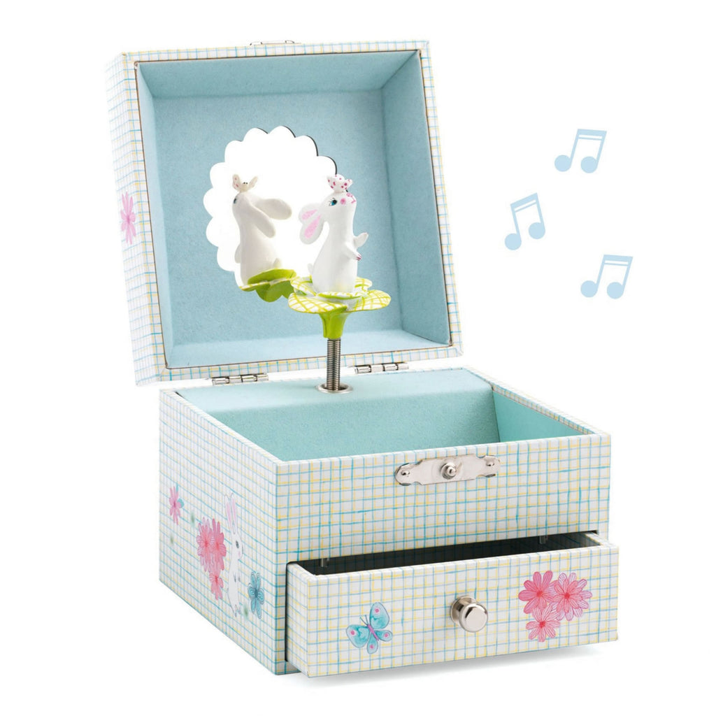 A decorative music box with a light blue and white gingham pattern, featuring a pink bunny on a green skirt inside an open lid, a drawer with a silver knob, and floating blue musical notes on a white background.