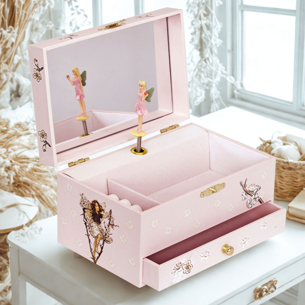 A pink decorative jewelry box with an open top drawer, floral and fairy illustrations, gold-tone hardware, and a mirror on the inside lid, shown on a white table in a bright room.