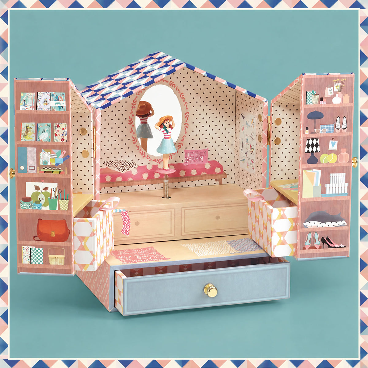 A dollhouse-style storage and play set with a pink polka-dot house frame, open shelves, drawers, and a small doll figure, photographed against a teal background with a decorative border.